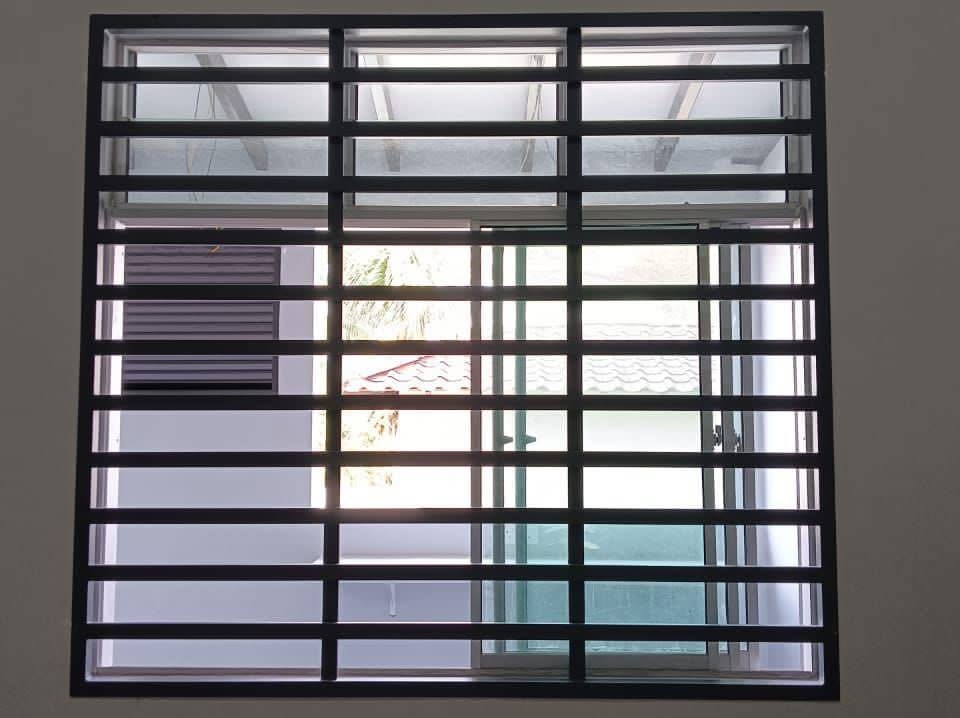 A black horizontal-bar security grille fitted over a sliding window with louvre vents, back-lit by daylight.