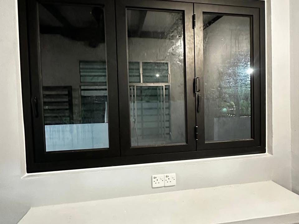 A fitted three-panel dark-framed aluminium casement window with lever handles, set in a white plastered wall.